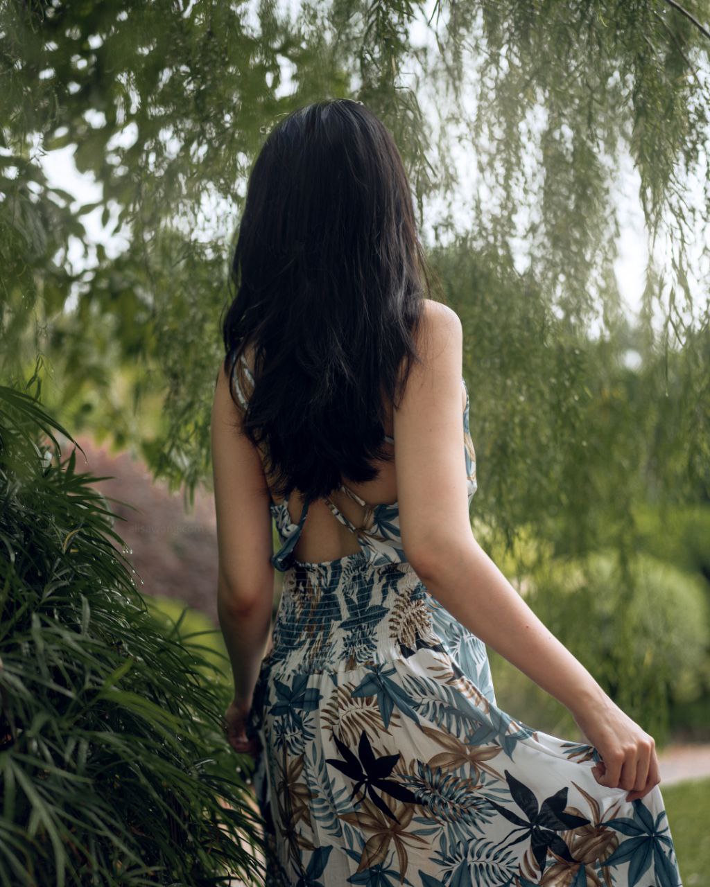 Back view of girl wearing a summer dress in a garden full of green plants