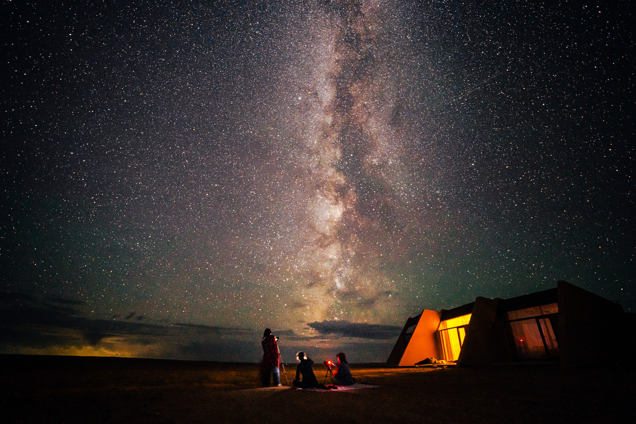 Group of people outside a lodge under a vast, starry sky